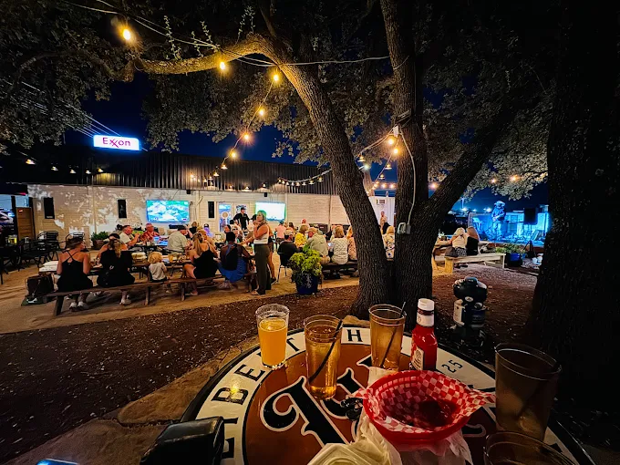 Liberty Hill Beer Market People gathered outdoors at night under string lights, enjoying food, drinks, and live music.